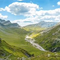 Blick auf die Greina-Ebene. èber den Bergen im Hintergrund ein bewölkter aber blauer Himmel.