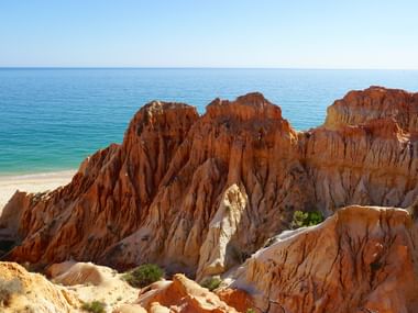 Berge Terracotta farbene Berge vor dem offenen blauen Meer, unter wolkenlosen blauen Himmel.