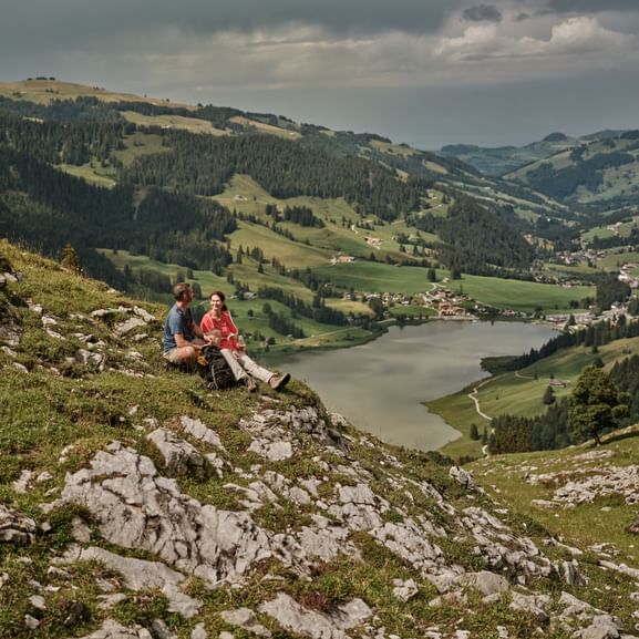 Ein Mann und eine Frau sitzen auf einem Hügel mit Blick auf einen See